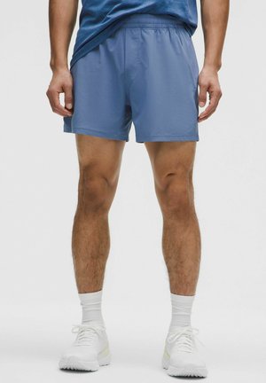 Pantaloni sportivi blu con un elastico in vita, caratterizzati da una superficie liscia e una vestibilità comoda. Indossati con scarpe da ginnastica bianche e calze.