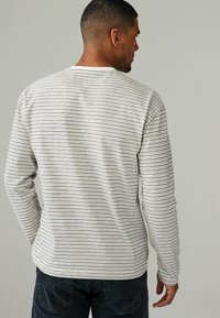 Langærmet skjorte i creme med tynde sorte striber, rund halsudskæring og tætsiddende ærmer. Blød tekstur med et afslappet design.