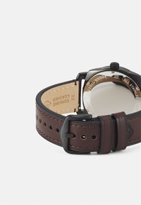 Brauner Lederarmband mit Perforationen, Gehäuse aus rostfreiem Stahl und schwarzen Akzenten; mit einem runden Ziffernblatt und Datumsanzeige.