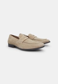 Beige Wildleder Slipper mit abgerundetem Zehenbereich, Mokassinstichdetails und einem niedrigen schwarzen Absatz. Mit einem gesteppten Riemen über dem Spann.
