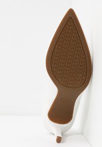 Semelle d'une chaussure blanche à bout pointu avec une bande de roulement marron ornée de logos "MK" répétés et un petit emblème "MK" près du talon.