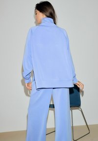 Lyseblåt afslapningstøjssæt med sweatshirt med høj krave og løs pasform, kombineret med vidde bukser; glat tekstur, minimale detaljer.