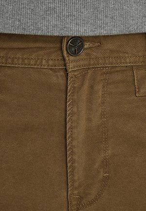 Pantalons en coton brun avec un tissage texturé, un bouton en métal et des coutures contrastantes le long de la taille et des poches.