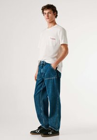 Valge puuvillane t-särk punase tekstiga taskul, koos lahtiste siniste teksadega, millel on suured esimesed taskud ja kontrastse õmblusega. Mustad tossud.