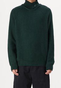 Dunkelgrüner Strickpullover mit hohem Kragen und Knopfdetail. Verfügt über gerippte Bündchen und Saum, aus weichem, strukturiertem Stoff.