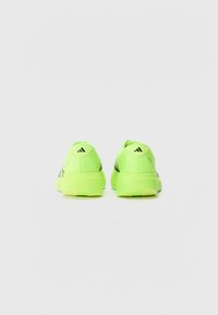 Zapatillas deportivas de color verde neón con un talón acolchado, tela texturizada y rayas de acento en negro. Presentan un logo en el talón. Diseño ligero.