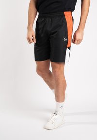 Schwarze Sportshorts mit seitlichen orangen und weißen Paneelen, elastischem Bund und Logodetails; leichtes, glattes Material, knielanger Schnitt.