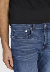 Slim-fit dżinsy w średnim niebieskim kolorze z wyblakłą teksturą, pięcioma kieszeniami, metalowymi elementami i kontrastowymi szwami.