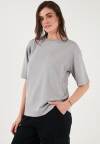 Šedé tričko s krátkým rukávem a kulatým výstřihem, vyrobené z hladké tkaniny. Má volný střih a minimální švy.