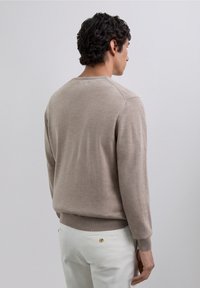 Beige gebreide trui met lange mouwen, ronde hals en geribbelde manchetten. Gladde textuur, lichtgewicht materiaal en subtiele naaddetails aan de achterkant.