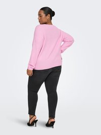 Pink knit sweater with a relaxed fit, long sleeves, and ribbed texture, paired with black skinny jeans and black heeled sandals.