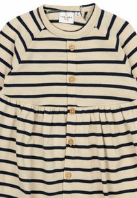 Bežinė suknelė su tamsiai mėlynomis juostomis, turinti apvalų kaklą, sagų priekinę dalį ir surinktą liemenį. Pagaminta iš minkštos, kvėpuojančios medžiagos.