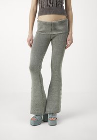 Pantalones de punto acampanados en gris claro, con una amplia cinturilla acanalada y acentos de botones laterales. Combinados con tacones de plataforma a juego.