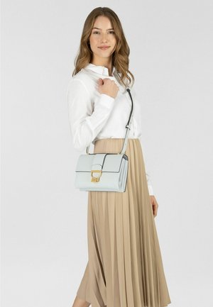 Bolso azul claro en cuero texturizado con un broche dorado, ribete negro y una correa larga ajustable, llevado con una falda plisada beige.