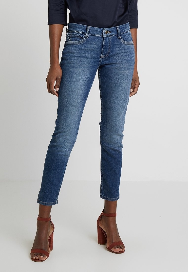 Smal passform blå denimjeans med medelhög midja, femficksdesign och lätt blekning. Kombinerat med bruna klacksandaler.