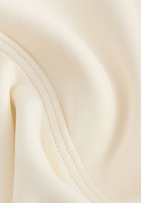 Cream-colored fabric with smooth texture and curved double stitching along one edge.