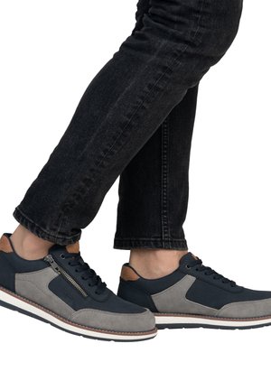 Blue and gray sneakers with a textured upper, featuring a zipper accent, white sole, and brown heel tab. Worn with dark jeans.