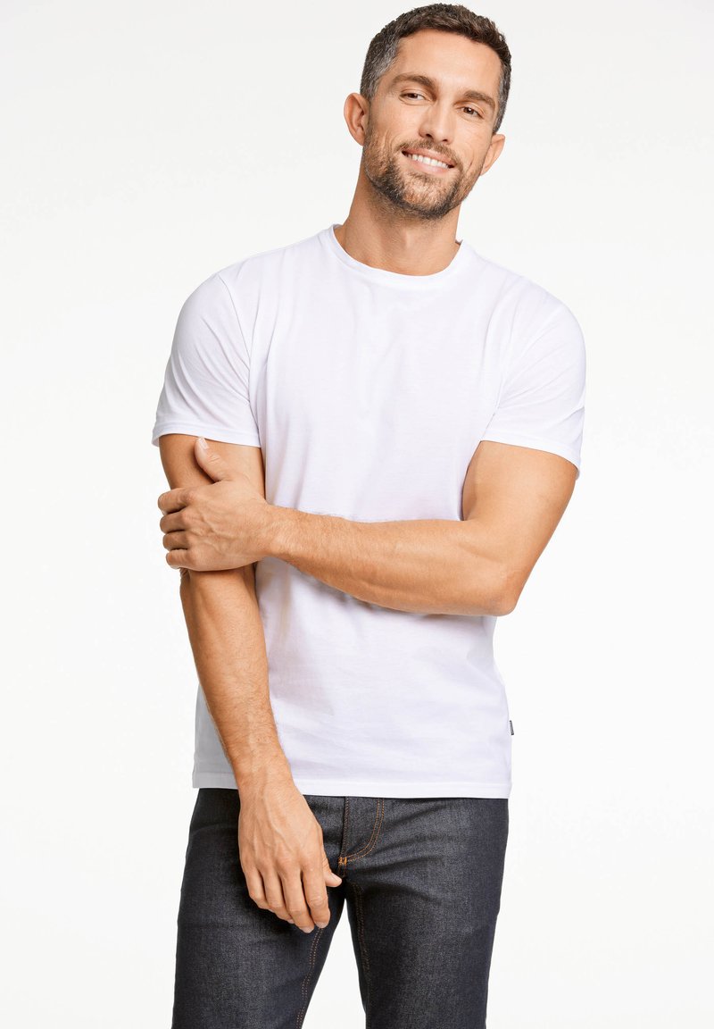 T-shirt bianco in cotone con maniche corte, scollatura a girocollo e vestibilità aderente, abbinato a jeans in denim scuri. Design semplice, senza motivi o grafiche.