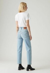 Ljust blå högmidjade jeans med rak ben, kombinerat med en vit t-shirt. Svarta ankelstövlar med klack. Denimtag synlig på baksidan.