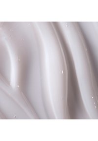 Lotion crémeux d'une teinte lavande claire, présentant une texture lisse et fluide avec un subtil éclat et de petites bulles à la surface.