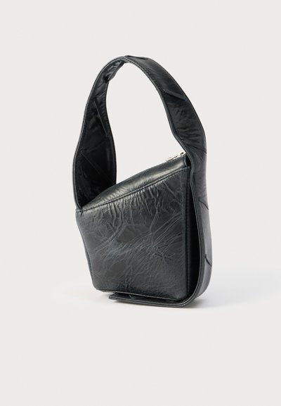 Μαύρη δερμάτινη τσάντα χειρός με φαρδιά τιράντα και δομημένο, ασύμμετρο σχέδιο, που στέκεται όρθια σε απλό λευκό φόντο.