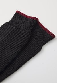 Calcetines de lana negros con un patrón texturizado, que presentan puños acanalados en burdeos en la parte superior. El diseño enfatiza la comodidad y la calidez.