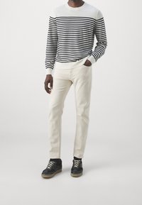 Suéter de rayas para hombre en blanco y negro, con mangas largas y escote redondo. Combinado con pantalones de color beige claro y zapatillas negras.
