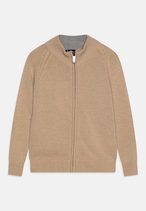 Cardigan beige en tricot avec fermeture éclair et col montant, intérieur gris contrastant. Doté de manches longues et de poignets et ourlet côtelés.