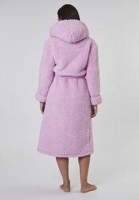 Rosa fluffig morgonrock med huva, långa ärmar, bälte och knä-lång design. Tillverkad av mjukt, texturerat material med en mysig känsla.