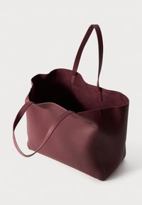 Bolsa tote de couro cor burgundy com um design minimalista, apresentando duas alças e um interior espaçoso e aberto com um acabamento texturizado.
