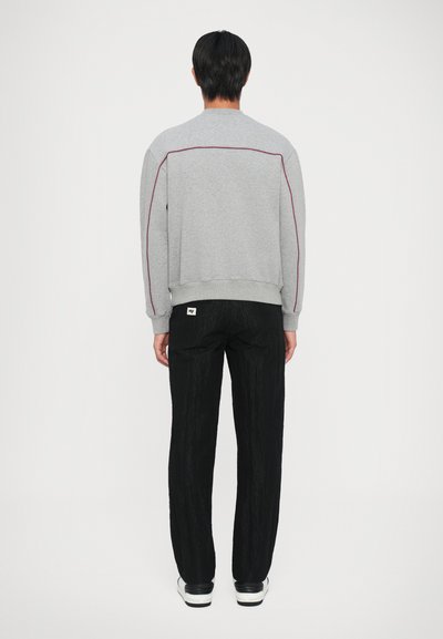 Felpa grigia con cuciture rosse, abbinata a pantaloni neri con texture. Il tessuto appare morbido e la vestibilità è rilassata. Sneakers bianche completano il look.