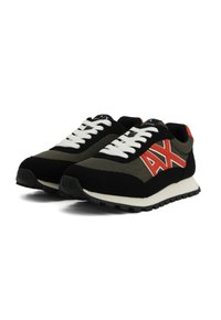Une paire de sneakers noires et olive avec des lacets blancs, un logo "AX" rouge sur les côtés, et de grosses semelles blanches sur un fond blanc.