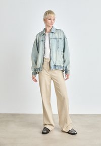 Lichtblauwe denim jas met elastische manchetten en zoom, gecombineerd met beige wijde broek en zwarte schoenen. Eenvoudig ontwerp, minimale details.