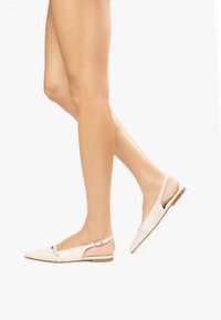 Scarpe slingback a punta in pelle sintetica bianca, con una decorazione a fibbia e suole piatte. Il design enfatizza una silhouette elegante.