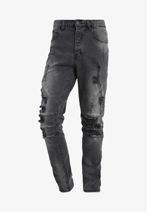 Zwarte distressed slim-fit jeans met meerdere scheuren en patch-details aan de voorkant, met een klassiek vijfzakkenontwerp en knoopsluiting.
