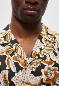 Καλοκαιρινό πουκάμισο κοντομάνικο σε μαύρο χρώμα, με λουλουδάτο μοτίβο σε ροζ, καφέ και τυρκουάζ. Διαθέτει κολάρο με εγκοπή και τσέπη στο στήθος. Μαλακή υφή υφάσματος.