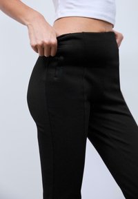 Leggings neri con una texture liscia, vita alta e una tasca laterale. Il tessuto appare elastico e aderente.