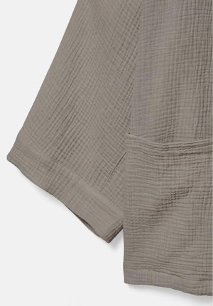 Tissu texturé brun clair avec coutures visibles et manchette retroussée, montrant un matériau doux, froissé, et des détails de couture.