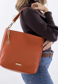 Orange læder skuldertaske med en glat overflade, guld hardware og et logokæde. Den har en bred silhuet og justerbar rem.