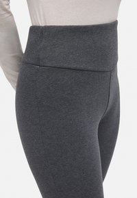 Leggings gris de talle alto, fabricados con un tejido suave y elástico, que presentan una textura lisa y líneas limpias sin costuras visibles.