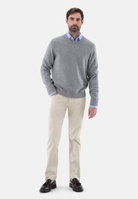 Grauer Pullover mit geripptem Saum über einem hellblauen Hemd mit Kragen, kombiniert mit beigen Hosen und schwarzen Slippers. Einfaches, klassisches Design.