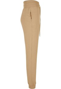Beige joggebukser laget av mykt stoff, med ribbet liv, snor, sidelommer og stramme mansjetter.