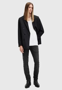 Schwarze, doppelt-knöpfbare, gestreifte Blazer mit großen Knöpfen, getragen über einem weißen T-Shirt und kombiniert mit schmalen schwarzen Jeans und Ankle Boots.
