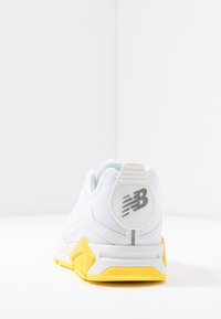 Baskets blanches avec une tige en maille texturée, semelle en caoutchouc jaune et logo gris sur le talon. Accent sur un design épuré et des accents vifs.