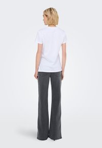 Camiseta blanca de algodón con mangas cortas, combinada con jeans de pierna ancha en gris. Los jeans cuentan con bolsillos traseros y un ajuste relajado.