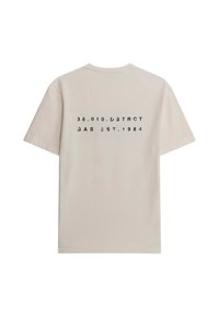 T-shirt beige a maniche corte con testo stampato in nero sulla schiena: "36.010.DṚSTRCT GAS EST.1984." Materiale cotone morbido.