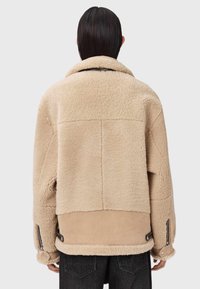 Beżowa kurtka z owczej wełny o puszystej teksturze, w oversize'owym kroju z widocznymi szwami. Posiada boczne zamki błyskawiczne oraz miękką zamszową dolną część.