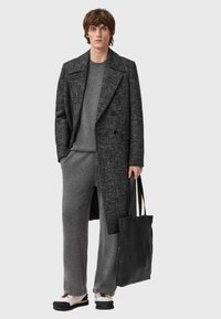 Szary wełniany płaszcz dwurzędowy na swetrze z dzianiny i szerokich spodniach w tym samym kolorze, zestawiony z czarną teksturowaną torbą typu tote i białymi trampkami.