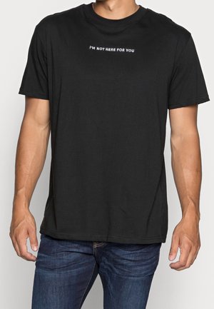 Schwarzes Baumwoll-T-Shirt mit kurzen Ärmeln, rundem Ausschnitt und weißem Text "I'M NOT HERE FOR YOU" auf der Brust.