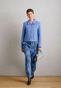 Ανοιχτό μπλε υφασμάτινο σακάκι με δύο μπροστινές τσέπες, συνδυασμένο με τζιν με σχέδια σε μπλε απόχρωση και γκρι τσάντα χειρός. Φορεμένο με μαύρα μποτάκια αστραγάλου.